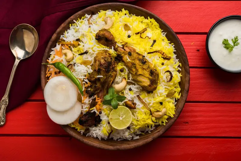 Chicken biryani with raita on a red table