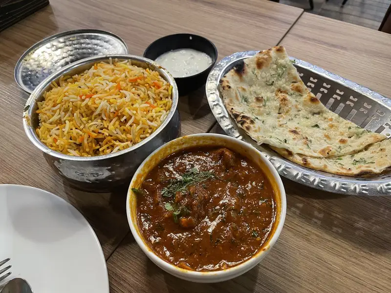 Biryani, curry and naan served in steel bowls